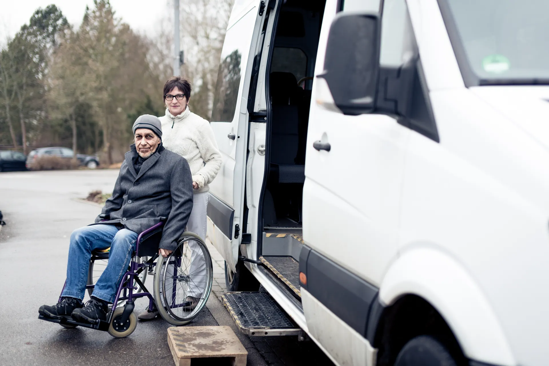 Personne en fauteuil roulant accompagnée devant un véhicule de transport adapté